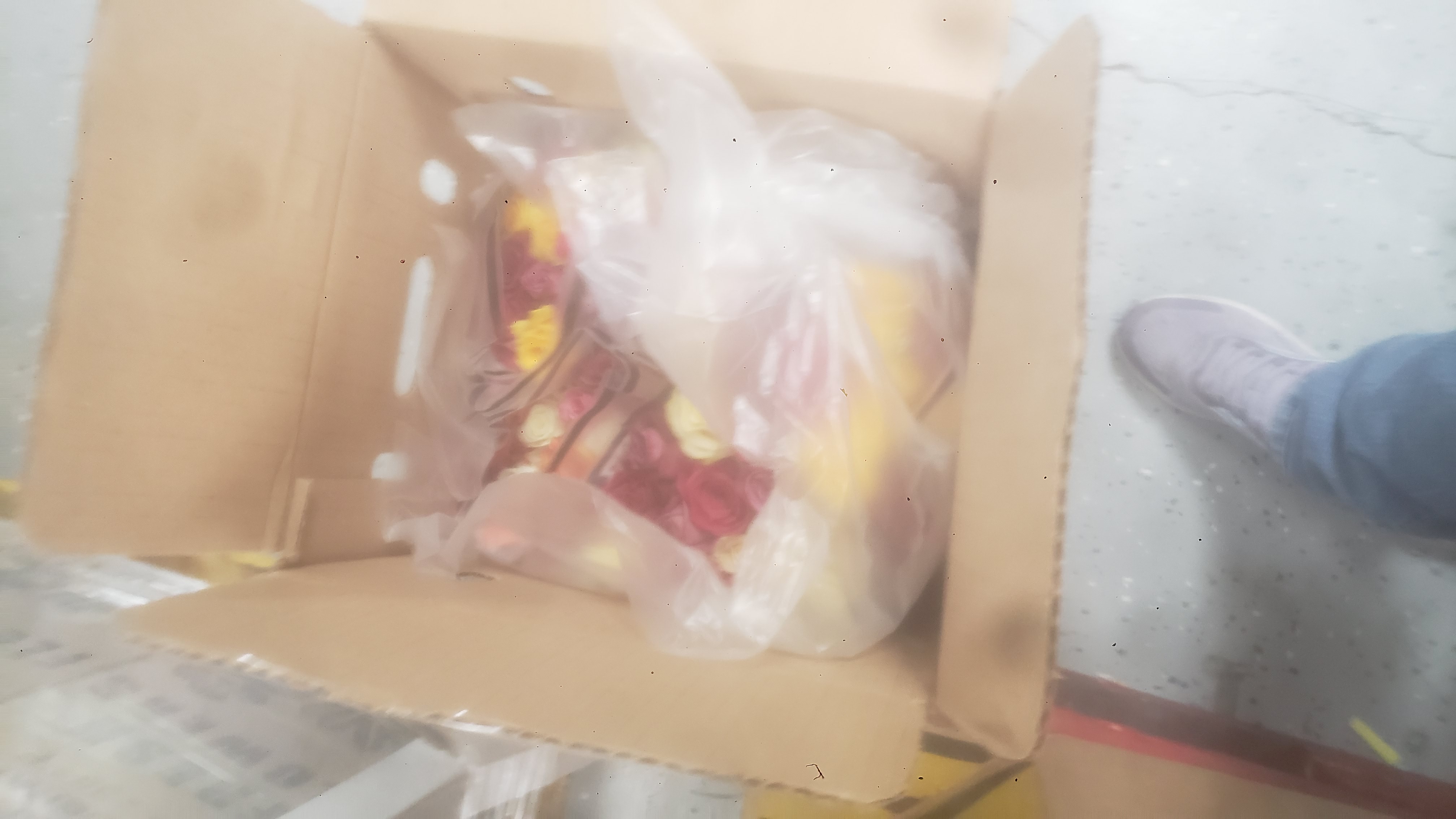 Bouquets of assorted roses in a plastic vase and long cardboard box.